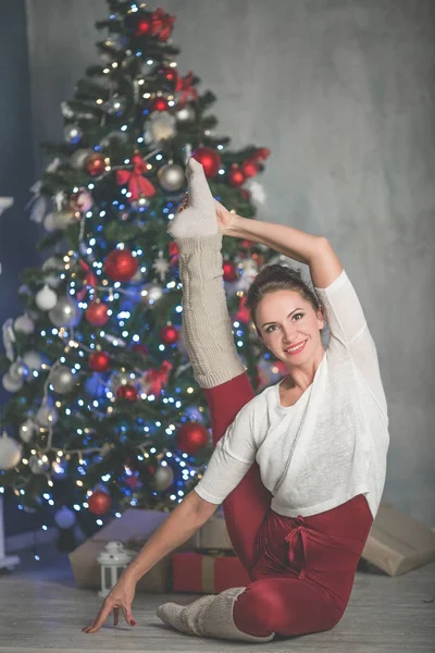 Αρκετά ευέλικτη γυναίκα κάνει διατάσεις κοντά στο χριστουγεννιάτικο δέντρο, σπορ και διακοπές έννοια — Φωτογραφία Αρχείου
