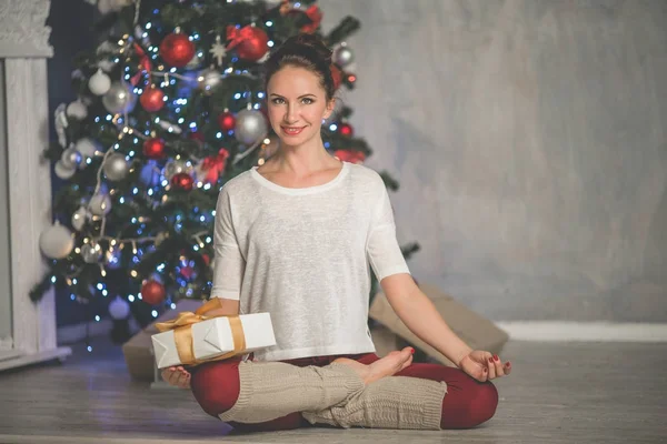 Hermosa mujer sonriente flexible está haciendo ejercicio de estiramiento cerca del árbol de Navidad de moda decorada en casa, deportes y concepto de vacaciones —  Fotos de Stock