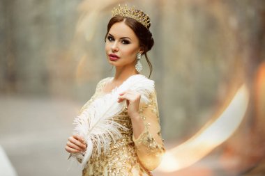 Güzel kadın moda makyaj ile Prenses lüks elbise ve beyaz tüy tutan taç giyiyor
