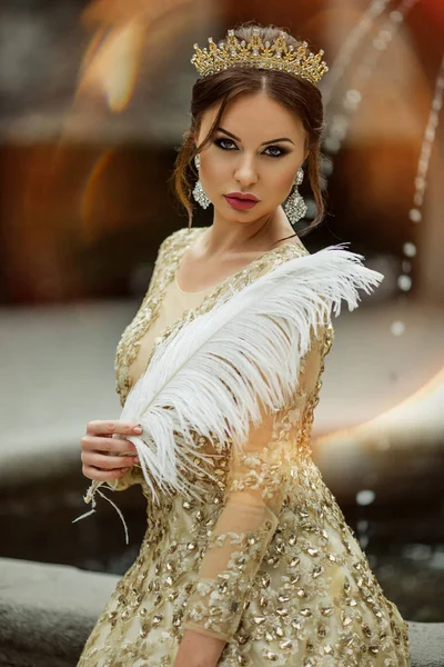 Vacker sexig kvinna med mode makeup bär prinsessa klä och krona håller vit fjäder — Stockfoto