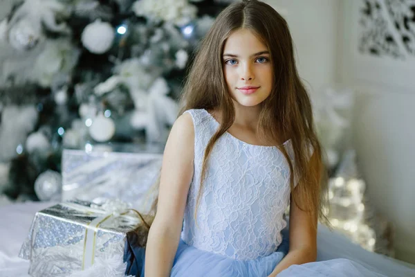 Portrét krásné dívky sedí poblíž nazdobený vánoční stromeček s stříbrná dárková krabička — Stock fotografie