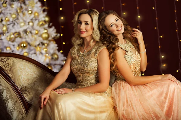 Красивые молодые мама и дочь носят модные золотые платья возле рождественского украшенного дерева — стоковое фото