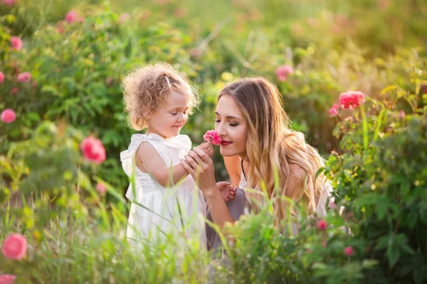 Vackra barn flicka med ganska ung mor vandrar i vårträdgård med rosa blomma rosor blommor — Stockfoto