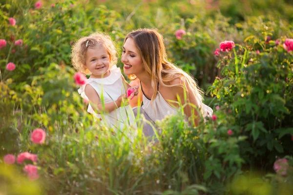 Mooie paar kind meisje met mooie jonge moeder lopen in lentetuin met roze bloesem rozen bloemen — Stockfoto