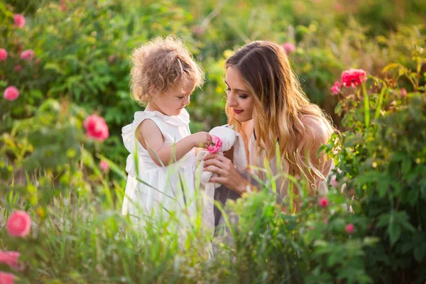 Mooie paar kind meisje met mooie jonge moeder lopen in lentetuin met roze bloesem rozen bloemen — Stockfoto