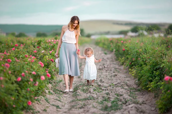 Frumos cuplu copil fata cu mama destul de tânără sunt de mers pe jos în grădină de primăvară cu flori roz trandafiri flori — Fotografie, imagine de stoc