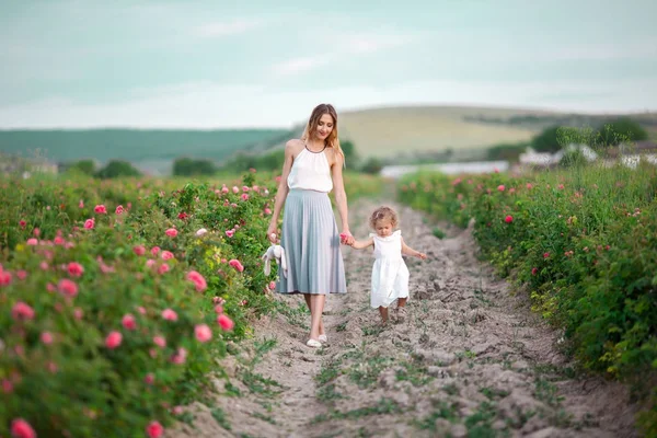 Frumos cuplu copil fata cu mama destul de tânără sunt de mers pe jos în grădină de primăvară cu flori roz trandafiri flori — Fotografie, imagine de stoc