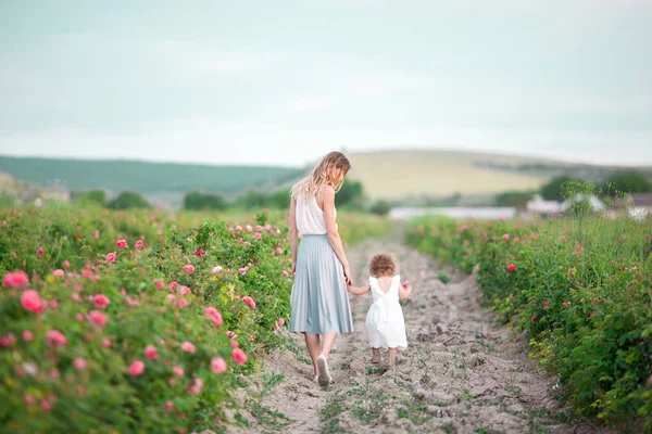 Frumos cuplu copil fata cu mama destul de tânără sunt de mers pe jos în grădină de primăvară cu flori roz trandafiri flori — Fotografie, imagine de stoc