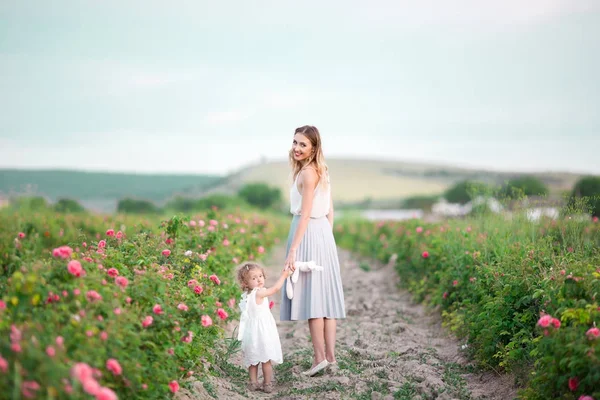 Frumos cuplu copil fata cu mama destul de tânără sunt de mers pe jos în grădină de primăvară cu flori roz trandafiri flori — Fotografie, imagine de stoc