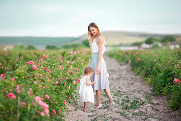 Beautiful couple child girl with pretty young mother are walking in spring garden with pink blossom roses flowers — Stock Photo, Image