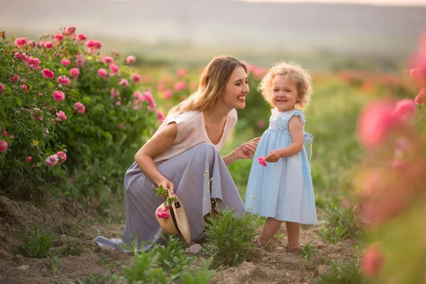 Beautiful couple child girl with mummy are walking in spring garden with pink blossom roses flowers — Stock Photo, Image