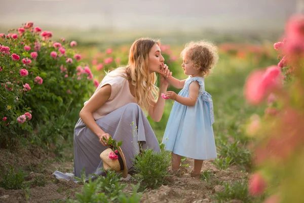 Bela menina casal criança com a mãe estão andando no jardim da primavera com flores rosa rosas flores, pôr do sol tempo — Fotografia de Stock