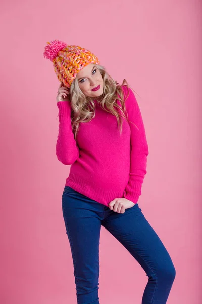 Beautiful young pregnant woman is wearing warm winter clothes hat and sweater isolated on pink background — Stock Photo, Image