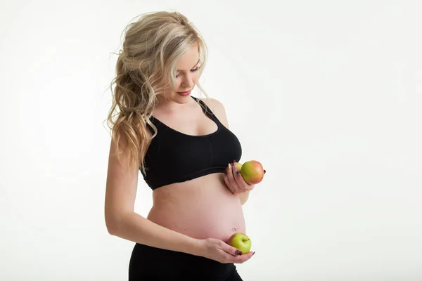 Schwangere schöne Frau trägt sportliche Kleidung mit grünen Äpfeln auf weißem, gesundem Essen — Stockfoto