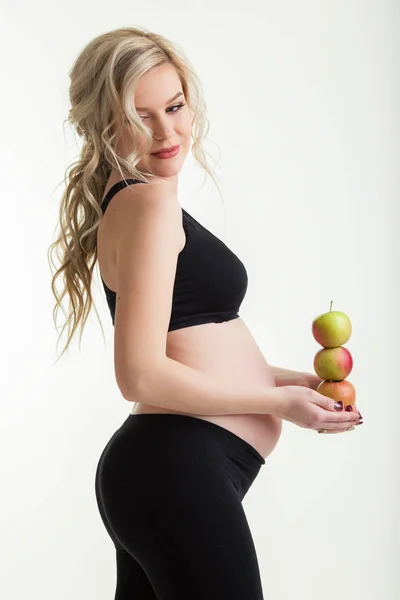 怀孕的美丽的女人穿着运动服持有绿色苹果孤立的白色, 健康的食物概念 — 图库照片