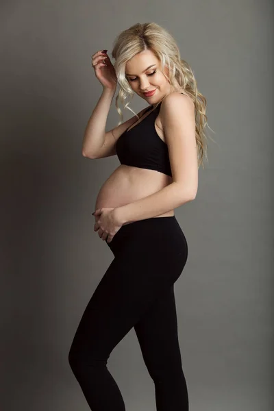 Embarazada hermosa mujer rubia está usando ropa deportiva negro aislado en gris, concepto de vida saludable — Foto de Stock