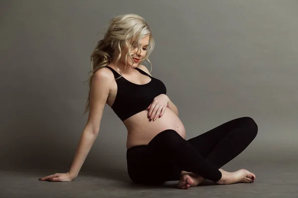 Femeie gravidă frumoasă blondă poartă haine negre sportive care fac exerciții de yoga izolate pe conceptul de viață gri și sănătos — Fotografie, imagine de stoc