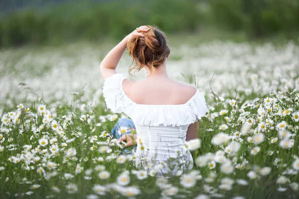 На задньому плані жінка на ромашковому полі носить білу сукню, весна — стокове фото