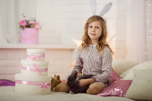 Pretty little girl at home is wearing bunny ears playing with rabbit — Stock Photo, Image