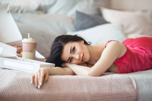 Gadis cantik berbaring di tempat tidur dan minum kopi dengan donat , — Stok Foto