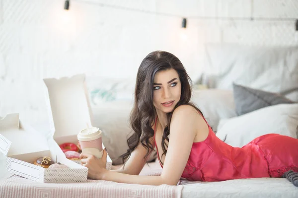 Bella ragazza è sdraiata a letto e bere caffè con ciambelle , — Foto Stock