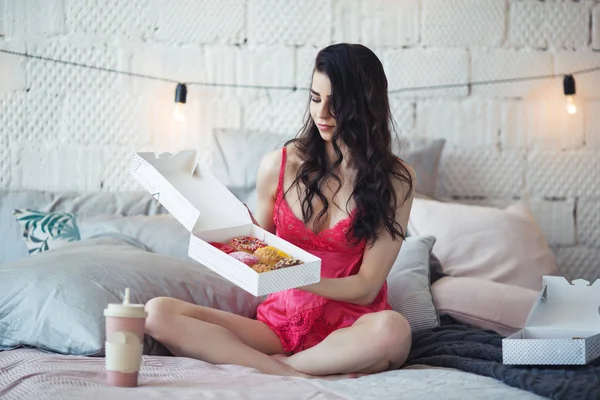 Menina bonita está sentada na cama com caixa de donuts doces, tempo de café da manhã, conceito de bom dia — Fotografia de Stock
