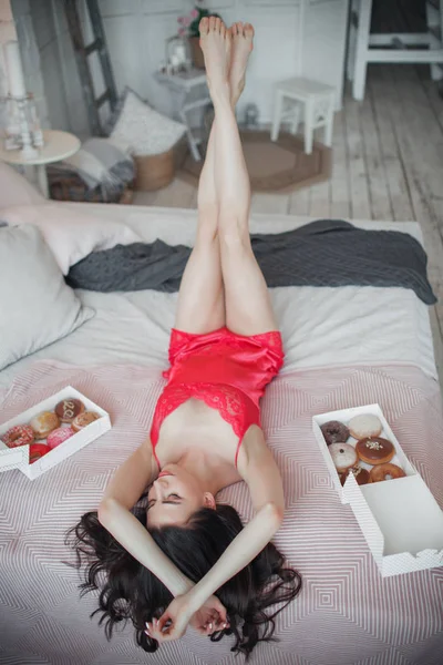 Bella ragazza sexy sottile è sdraiata a letto con ciambelle dolci, ora di colazione, concetto di buongiorno — Foto Stock