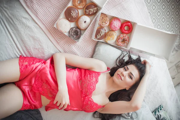 Menina bonita está deitada na cama com donuts doces, tempo de café da manhã, conceito bom dia — Fotografia de Stock