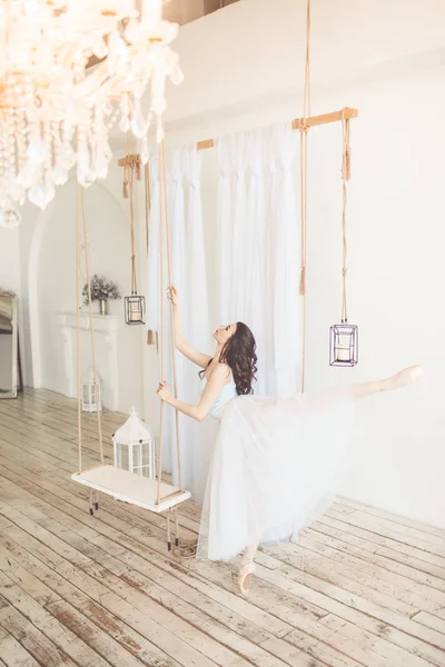 Young pretty ballerina is dancing near swing in studio with light interior — Stock Photo, Image