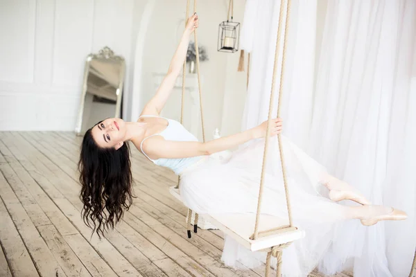 Молода красива балерина сидить на гойдалках і розважається в студії — стокове фото