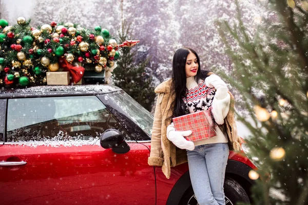 Pretty young girl near red car with decorated xmas tree. — Stock Photo, Image