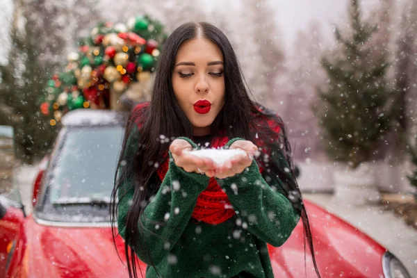 예쁜 여자 애가 빨간 차 옆에서 크리스마스 트리 장식을 하고 눈 놀이를 하고 있어요. — 스톡 사진