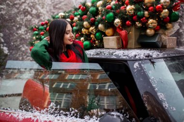Güzel genç kız çatıda süslü Noel ağacı olan kırmızı arabanın yanında duruyor, tatil konsepti..