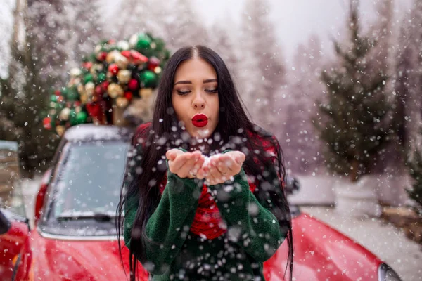 Pretty young girl is playing with snow near red car with decorated xmas tree. — Stock Photo, Image