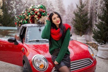 Güzel genç kız çatıda süslü Noel ağacı olan kırmızı arabada oturuyor, tatil konsepti..