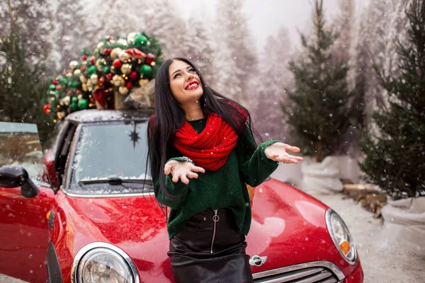 Όμορφη νεαρή κοπέλα παίζει με το χιόνι κοντά στο κόκκινο αυτοκίνητο με διακοσμημένο χριστουγεννιάτικο δέντρο. — Φωτογραφία Αρχείου