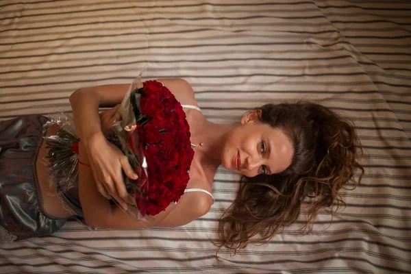 Goede morgen Aantrekkelijke jonge vrouw in bed houdt boeket van honderd rode rozen. — Stockfoto