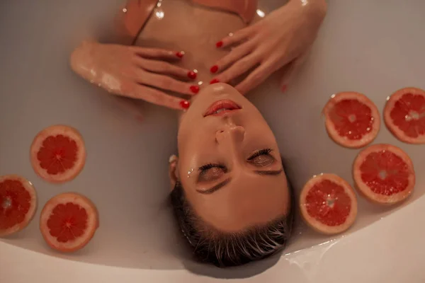 Portrét sexy ženy ve vaně s mlékem a kruhy z grapefruitu — Stock fotografie