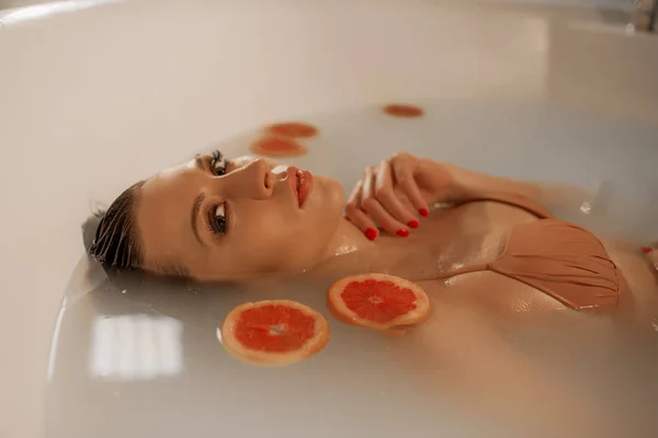 Sexy young woman with perfect skin in a bath with milk and circles of grapefruit