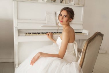 Güzel elbiseli genç gelin, parlak beyaz stüdyoda piyano çalıyor. Düğün konsepti.