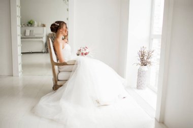 Lüks elbiseli genç gelin parlak beyaz stüdyoda bir buket çiçek tutuyor. Düğün moda konsepti.