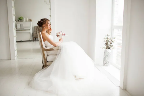 明るい白いスタジオで花の花束を保持する美しいドレスで若い花嫁。結婚式のコンセプト. — ストック写真