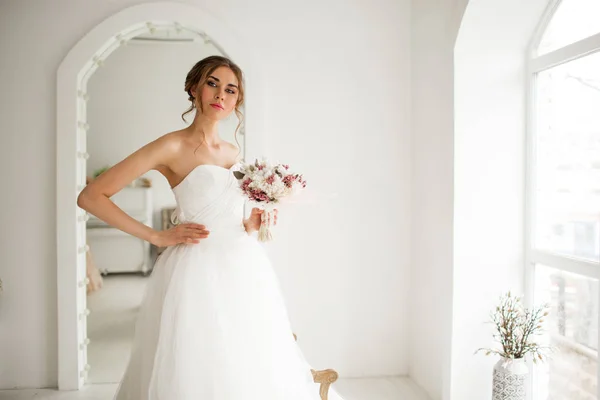 Молода наречена в красивій сукні тримає букет квітів у яскраво-білій студії. Весільна концепція . — стокове фото