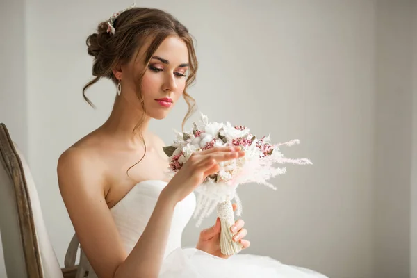 Primer plano retrato de la novia joven en un hermoso vestido con un ramo de flores en un estudio de color blanco brillante. Concepto de boda . — Foto de Stock