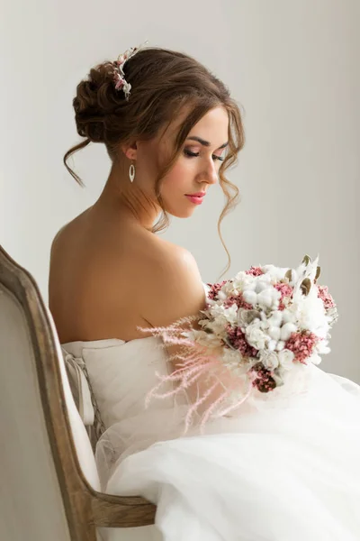 Primer plano retrato de la novia joven en un hermoso vestido con un ramo de flores en un estudio de color blanco brillante. Concepto de boda . — Foto de Stock