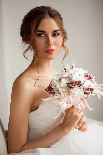 Primer plano retrato de la novia joven en un hermoso vestido con un ramo de flores en un estudio de color blanco brillante. Concepto de boda . — Foto de Stock