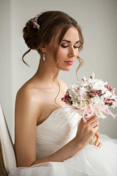 Крупним планом портрет молодої нареченої в красивій сукні, що тримає букет квітів у яскраво-білій студії. Весільна концепція . — стокове фото