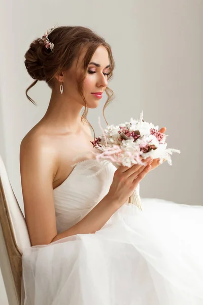 Close up portrait of young bride in a beautiful dress holding a bouquet of flowers in bright white studio. Wedding concept. — Stock Photo, Image