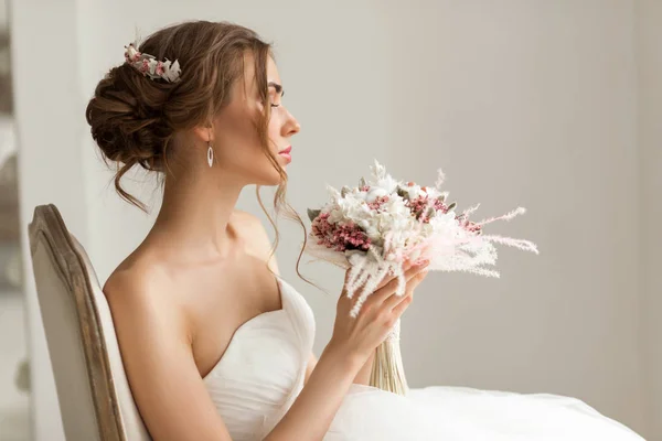 Primer plano retrato de la novia joven en un hermoso vestido con un ramo de flores en un estudio de color blanco brillante. Concepto de boda . — Foto de Stock