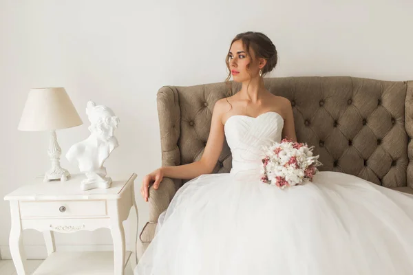 Joven novia en un hermoso vestido sentado en casa con un bonito interior blanco. Concepto de boda . — Foto de Stock